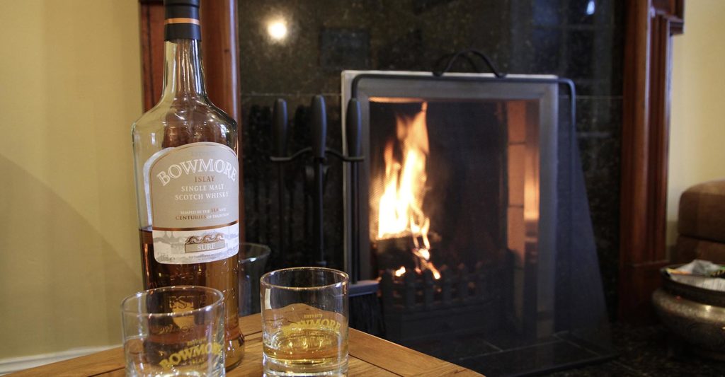 A bottle of whisky in front of a fireplace at Dundonald cottage, Islay Cottages