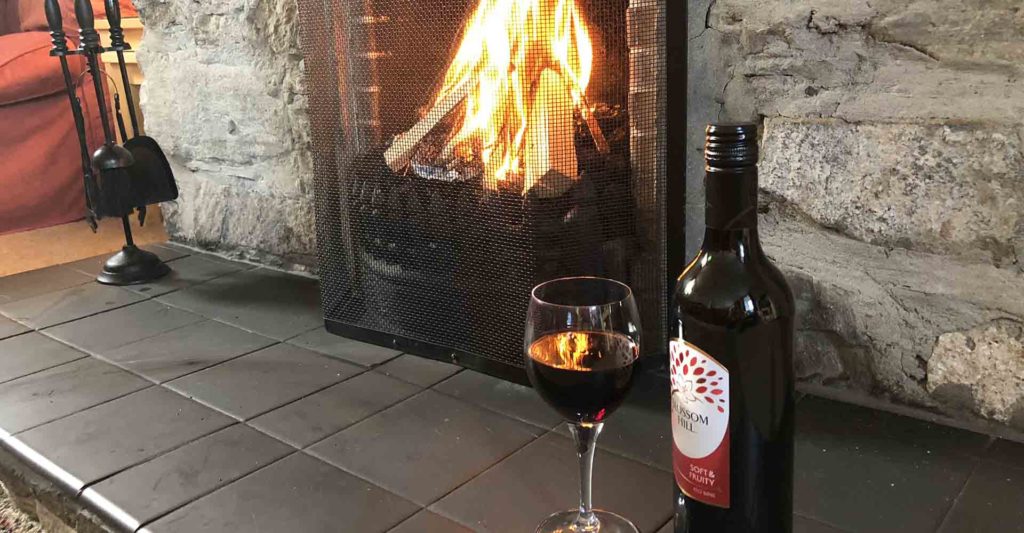 A bottle and glass of red wine by a roaring fire in Machir Cottage at Islay Cottages