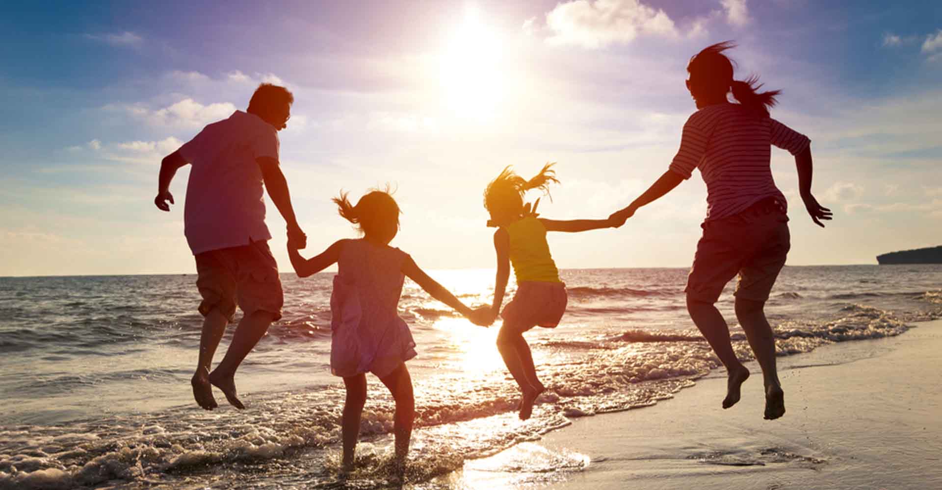 Family holding hands and splashing in water on the beach