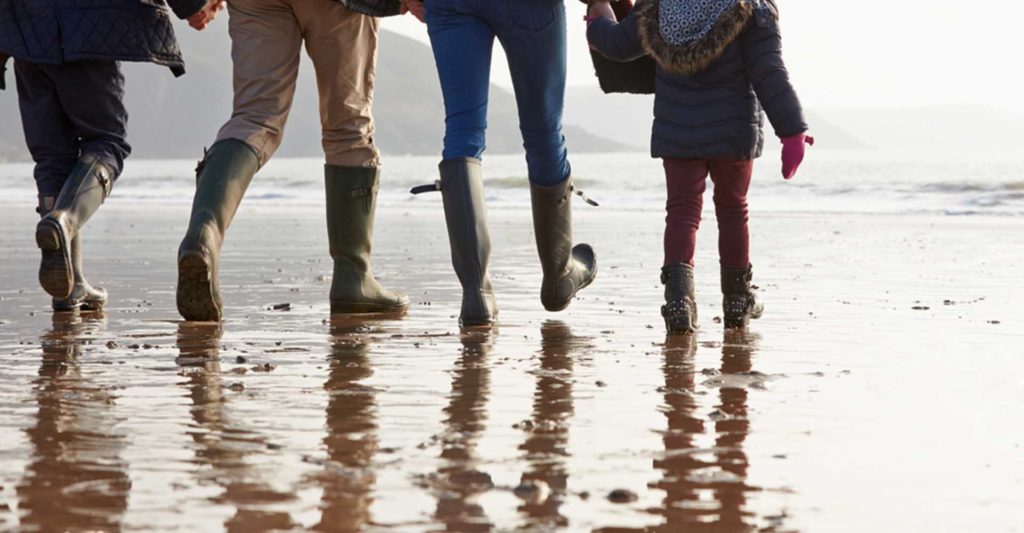 A family in warm clothing and wellies walking on a beach