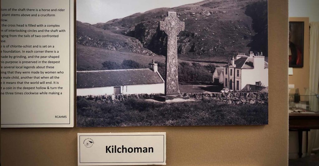 A picture of the Celtic Cross at Kilchoman with Kilchoman House in the backgroud at the Port Charlotte Museum on Islay