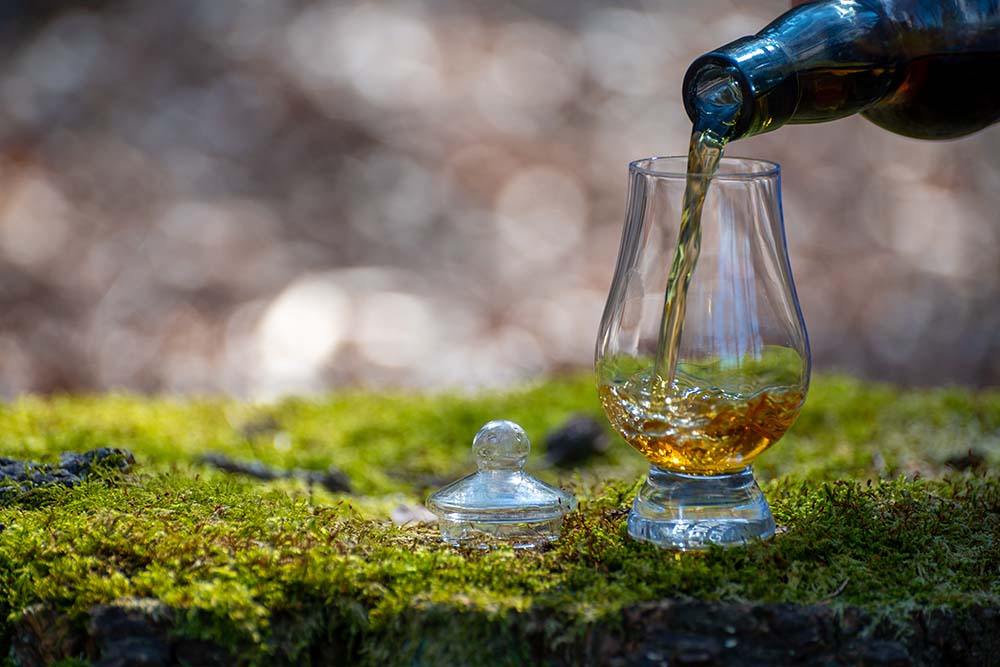 Pouring a glass of whisky on mossy stones.
