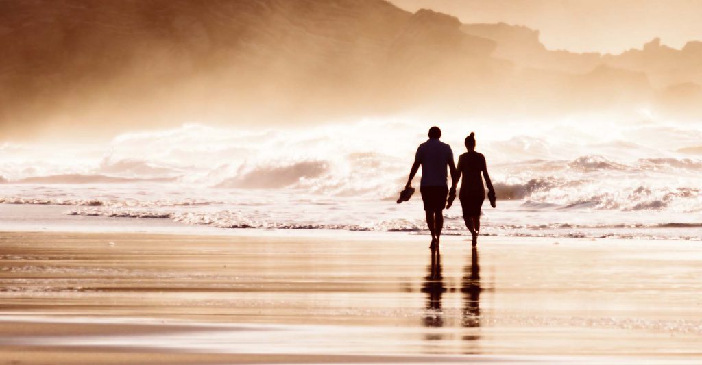 A couple having a romantic stroll on the beach at sunset